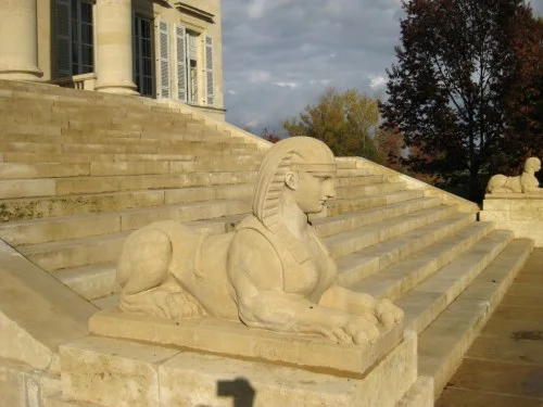 2008-11-6に酒井 浩（プラチナワイン（有限会社デリバリー・ワイン）代表）がボルドー、メドック地区、マルゴー村、シャトー・マルゴーで撮影したシャトー本館の階段脇に鎮座するスフィンクス像。新古典主義建築の優美なディテールと、背後に広がる新緑のコントラストが印象的です