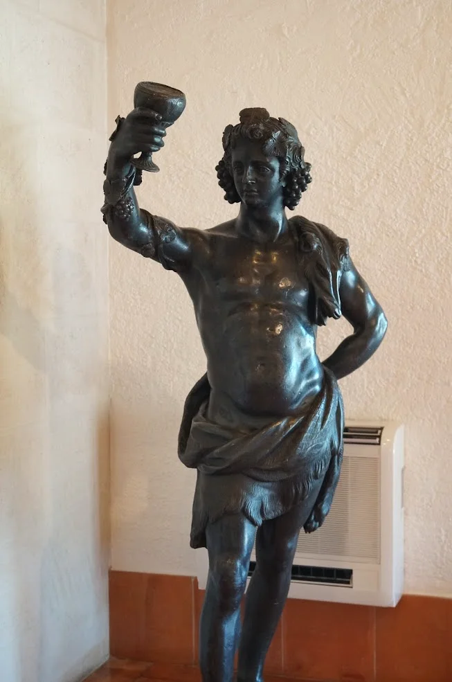 2013-04-29に酒井 浩（プラチナワイン（有限会社デリバリー・ワイン）代表）がシャトー・ムートン・ロートシルト / Pauillac, Médoc, Bordeaux, Franceで撮影したワイン杯を高く掲げるブドウ酒の神バッカスのブロンズ像。ブドウの葉と房の冠を纏いシャトー玄関ホールに鎮座する。ロスチャイルド家の美術コレクションの一端を示す装飾。