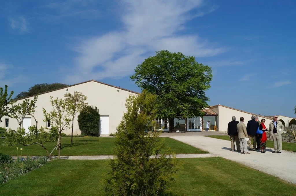 2013-04-29に酒井 浩（プラチナワイン（有限会社デリバリー・ワイン）代表）がシャトー・ムートン・ロートシルト / Pauillac, Médoc, Bordeaux, Franceで撮影したチャイ（樽熟成庫）前の中庭に集い、ガイドの説明に耳を傾ける訪問者グループ。中央に枝を広げる巨大な落葉樹の緑陰が心地よく、奥にはチャイ入口と作業場の白い建物が見え