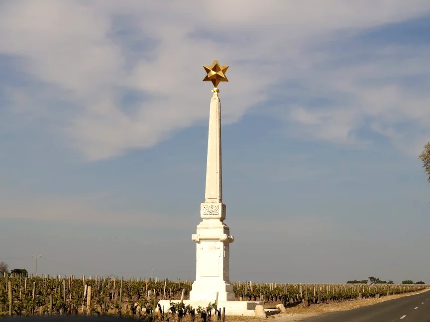 2013-04-29に酒井 浩（プラチナワイン（有限会社デリバリー・ワイン）代表）がシャトー・ムートン・ロートシルト / Pauillac, Médoc, Bordeaux, Franceで撮影したメドック街道沿いに立つ、ロスチャイルド家の紋章であるダビデの星（六芒星）を頂くシャトー境界標識のオベリスク。周囲には剪定されたブドウ樹が広がり、春のポイヤック葡